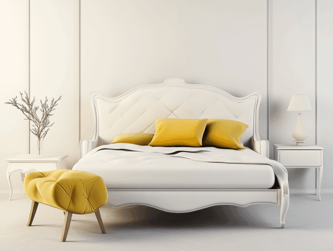 Ein modernes Schlafzimmer mit einem weißen, verschnörkelten französischen Bettgestell, weißer Bettwäsche und gelben Akzent-Kissen. Eine passende gelbe gepolsterte Bank steht am Fußende des Bettes. Auf den weißen Nachttischen stehen eine Lampe und ein dekorativer Zweig.
