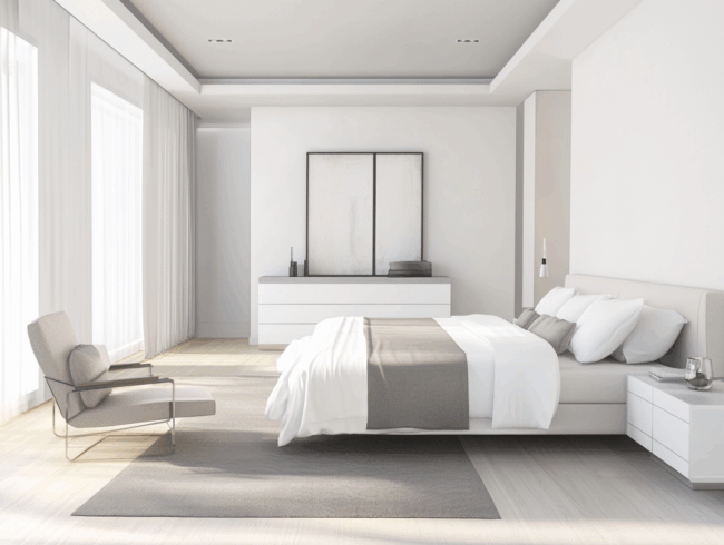 Ein modernes, minimalistisches Schlafzimmer mit einer hellen Farbpalette, mit einem ordentlich gemachten Bett mit Matratzen für Allergiker, einem grauen Teppich, einem Sessel, einer Kommode mit gerahmter Kunst und großen Fenstern mit transparenten Vorhängen, die natürliches Licht hereinlassen.