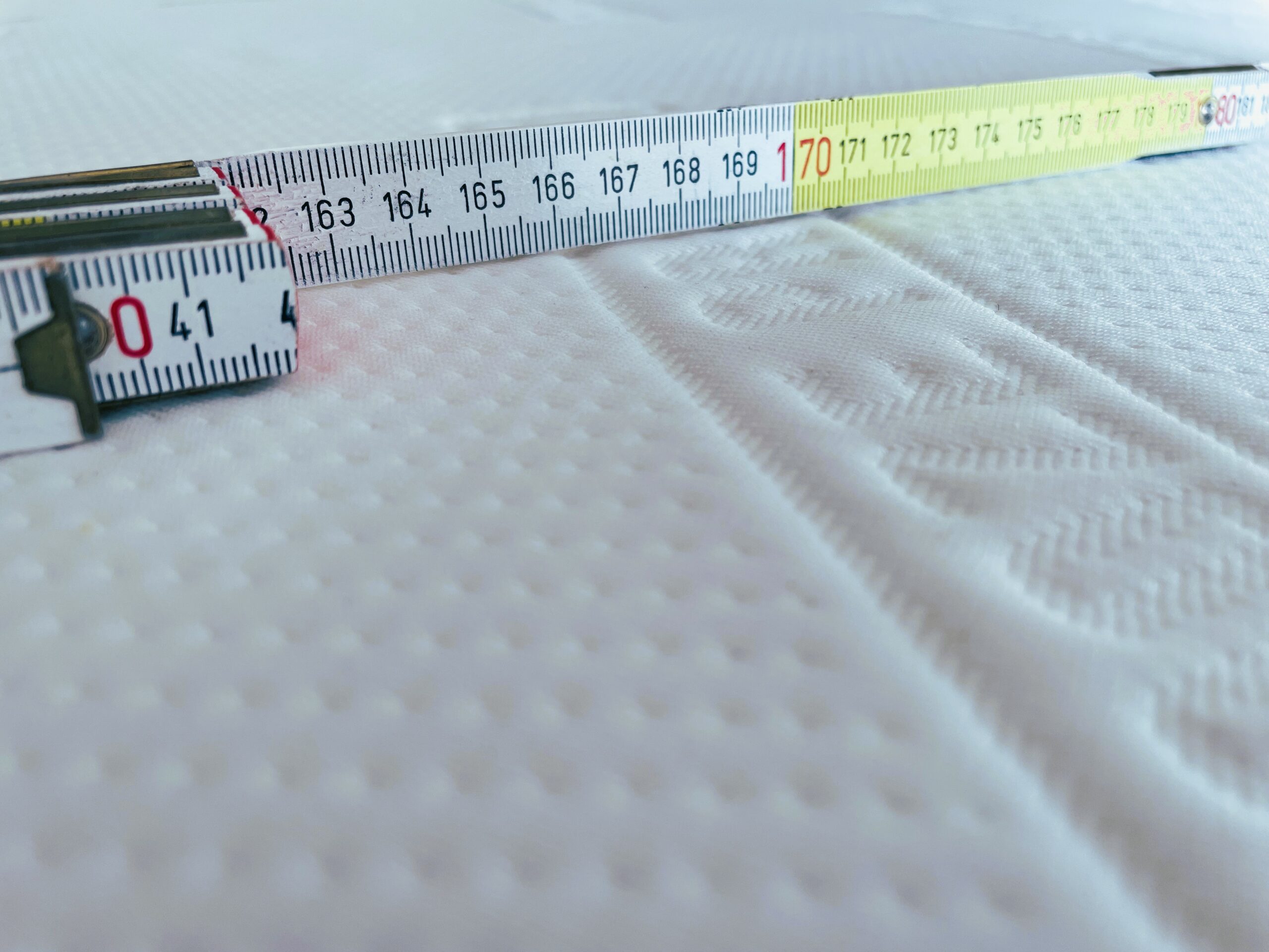 Nahaufnahme eines Maßbandes, das über eine weiße, strukturierte Oberfläche gelegt wurde und Messungen um die 170 cm-Marke zeigt.