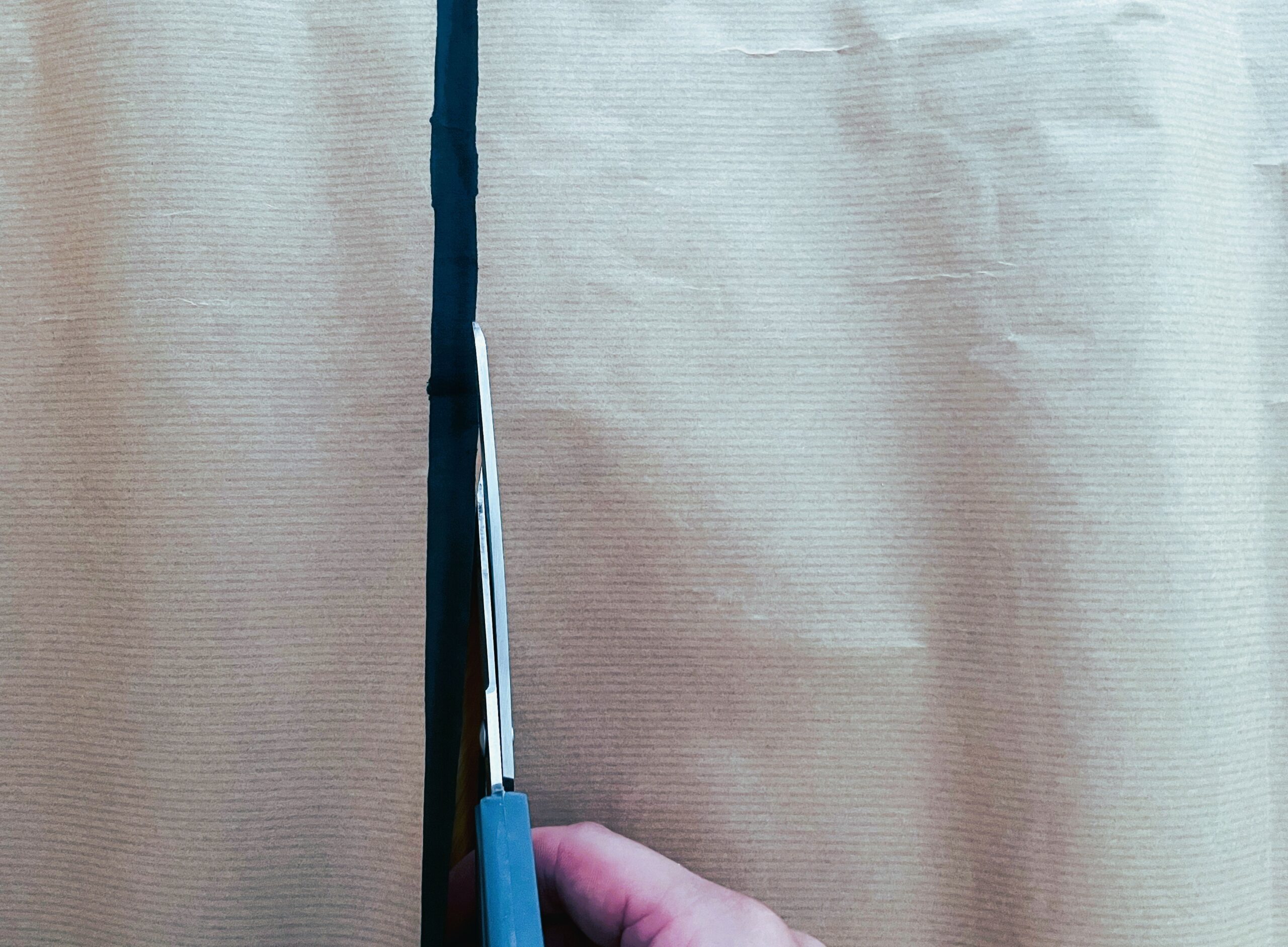 Eine Hand, die eine Schere hält, schneidet entlang einer schwarzen Linie, die auf einem Blatt braunen Kraftpapiers gezeichnet ist.