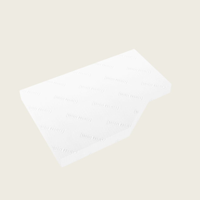 Eine rechteckige, weiße Matratzenauflage mit einem leicht schrägen Schnitt auf einer Seite, die vor einem schlichten, cremefarbenen Hintergrund abgebildet ist. Die Oberfläche weist ein dezentes, sich wiederholendes Muster mit schwachem Text auf.