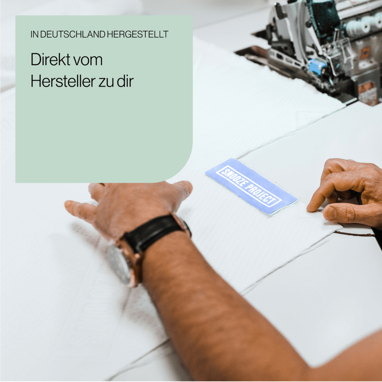 Eine Person ordnet ein blaues Etikett mit der Aufschrift STÜLZ PROJECT auf weißem Stoff neben einer Nähmaschine an. Der Text auf Deutsch lautet: In Deutschland hergestellt. Direkt vom Hersteller zu dir.