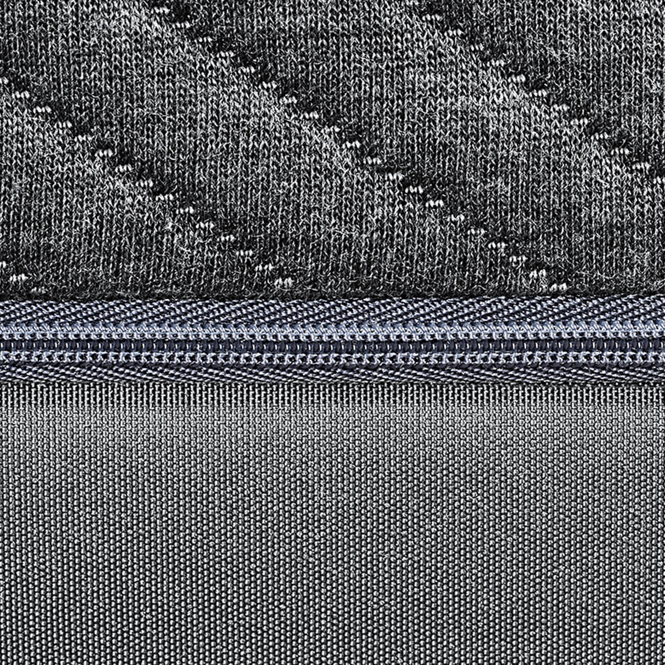 Nahaufnahme eines strukturierten grauen Stoffes mit einem diagonalen Strickmuster oben, das in der Mitte durch einen Reißverschluss getrennt ist, und einem glatteren Webstoff unten.