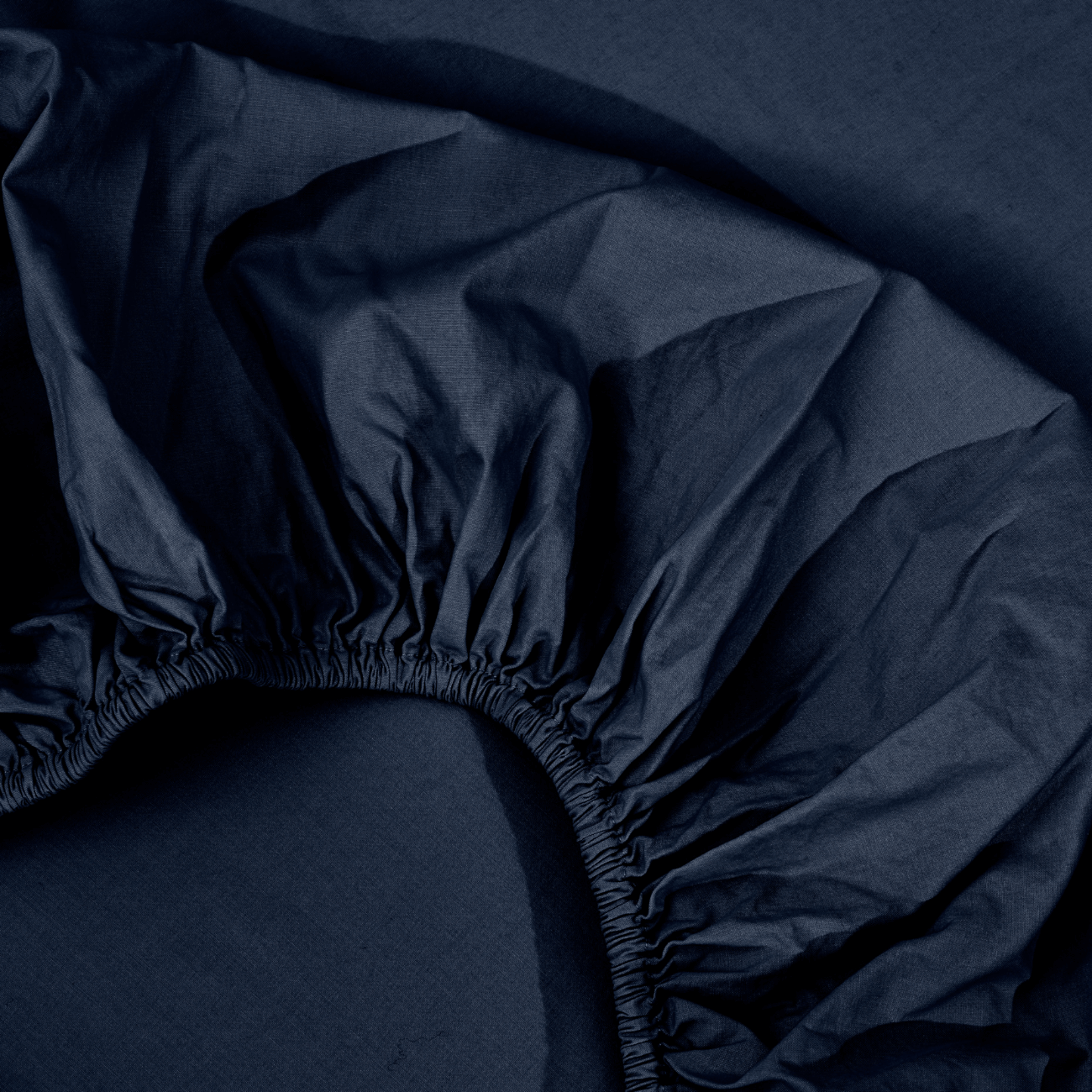 spannbettlaken nach maß blau 2 Nahaufnahme eines dunkelblauen Spannbettlakens mit gerafften Gummirändern, ausgebreitet auf einem Bett.