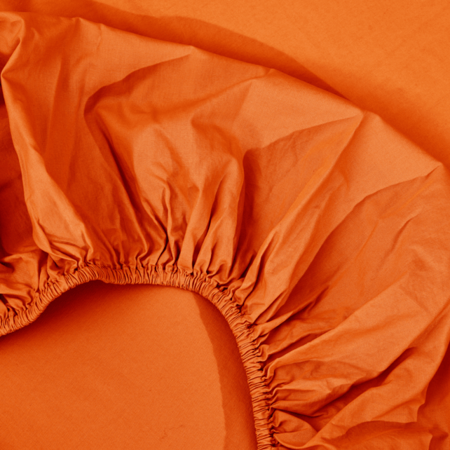 Eine Nahaufnahme eines orangefarbenen Spannbettlakens mit sichtbaren elastischen Rändern, das auf einer orangefarbenen flachen Oberfläche ausgebreitet ist.