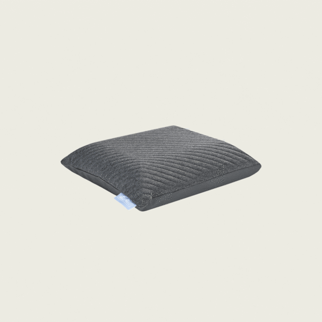 Ein dunkelgraues, quadratisches Kissen mit einer gerippten Struktur auf der Oberseite und einem kleinen blauen Etikett an der Seite, vor einem schlichten hellen Hintergrund.