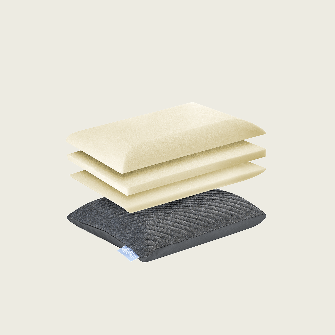Snooze-Project-Pillow-02_04 Ein Kissen aus Memory-Schaumstoff, dessen Schichten getrennt und darüber gestapelt sind, mit drei cremefarbenen Schaumstoffschichten und einem dunkelgrauen Stoffbezug mit einem kleinen blauen Etikett auf einem schlichten hellen Hintergrund.