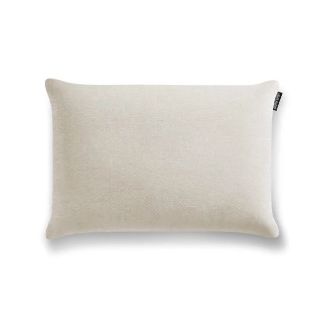 Ein rechteckiges, hellbeiges Soft-Canvas-Kissen mit dezenter Textur und kleinem schwarzen Anhänger ist auf einem weißen Hintergrund platziert. Dieses Viscoschaum Deko-Kissen fügt Komfort und Stil mit seiner sanften Schlaffunktion hinzu.