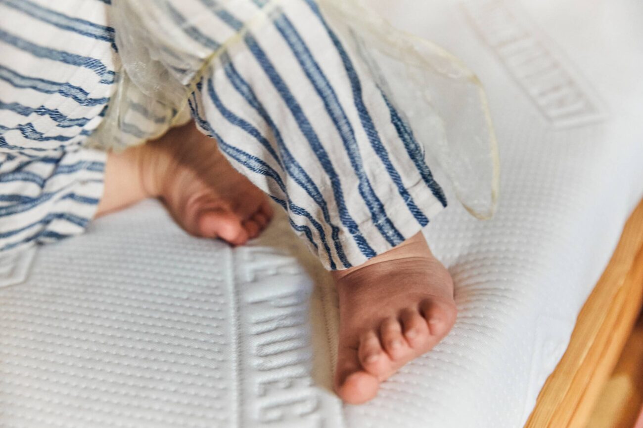 Nahaufnahme eines Kindes mit nackten Füßen und gestreiften Hosen auf einer strukturierten weißen Matratzenoberfläche, die einen gemütlichen Familienbett-Moment einfängt.