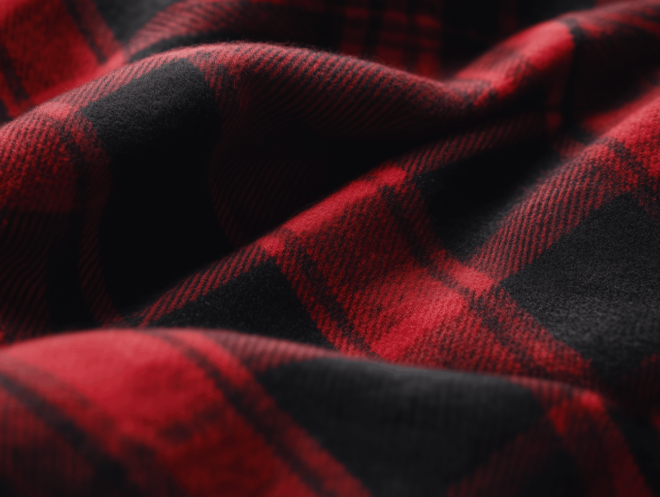 Nahaufnahme eines weichen, rot-schwarz karierten Flanellstoffs mit sanften Falten, der ein klassisches Schottenmuster und eine warme, gemütliche Textur aufweist.
