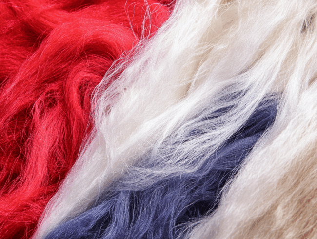 Nahaufnahme von langen, weichen Kunstfasern in roten, weißen und blauen Farben, die nebeneinander angeordnet sind und an Strähnen aus gefärbter Wolle oder Kunsthaar erinnern.