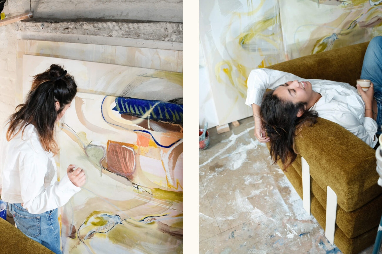 Eine Frau mit dunklem Haar, weißem Hemd und Jeans malt eine abstrakte Leinwand, dann entspannt sie sich auf einer grünen Couch mit einer Tasse in der Hand, umgeben von Kunstzubehör und bemalten Böden.