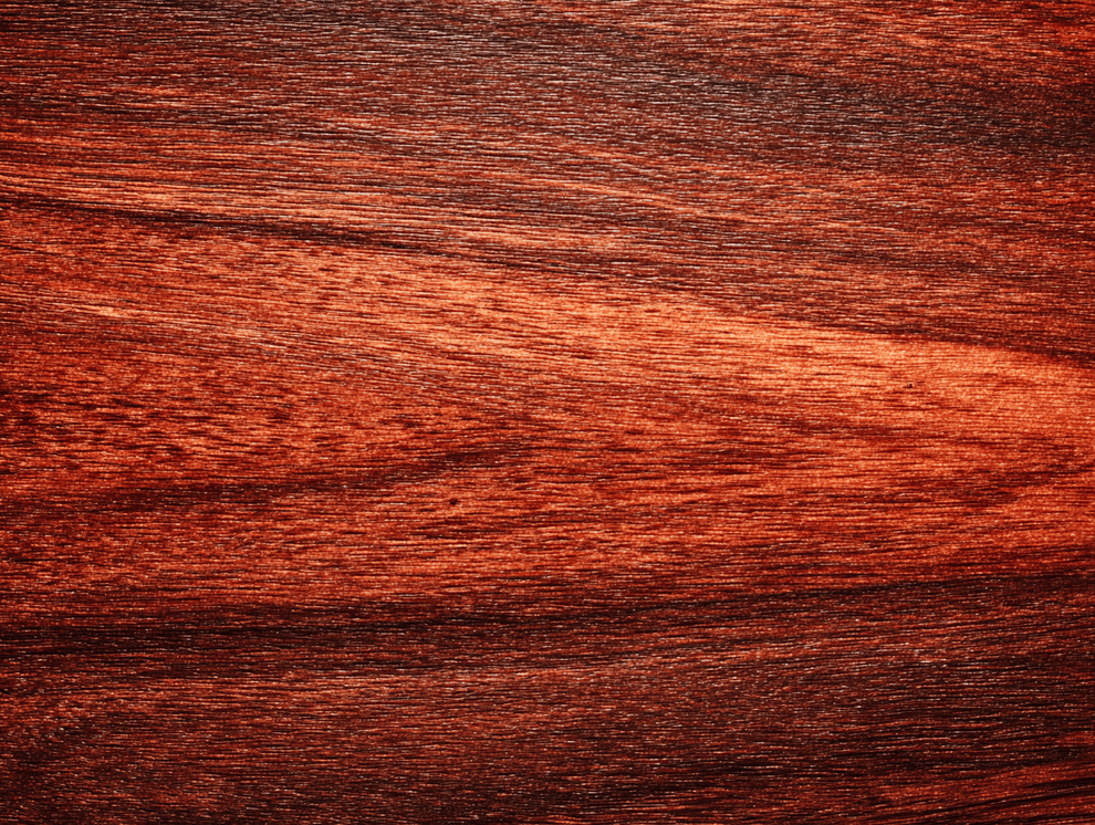 Nahaufnahme einer polierten Mahagoni-Holzoberfläche mit satter, rötlich-brauner Farbe und natürlichen, horizontal verlaufenden Maserungen. Die Textur und der Glanz des Holzes sind deutlich sichtbar.