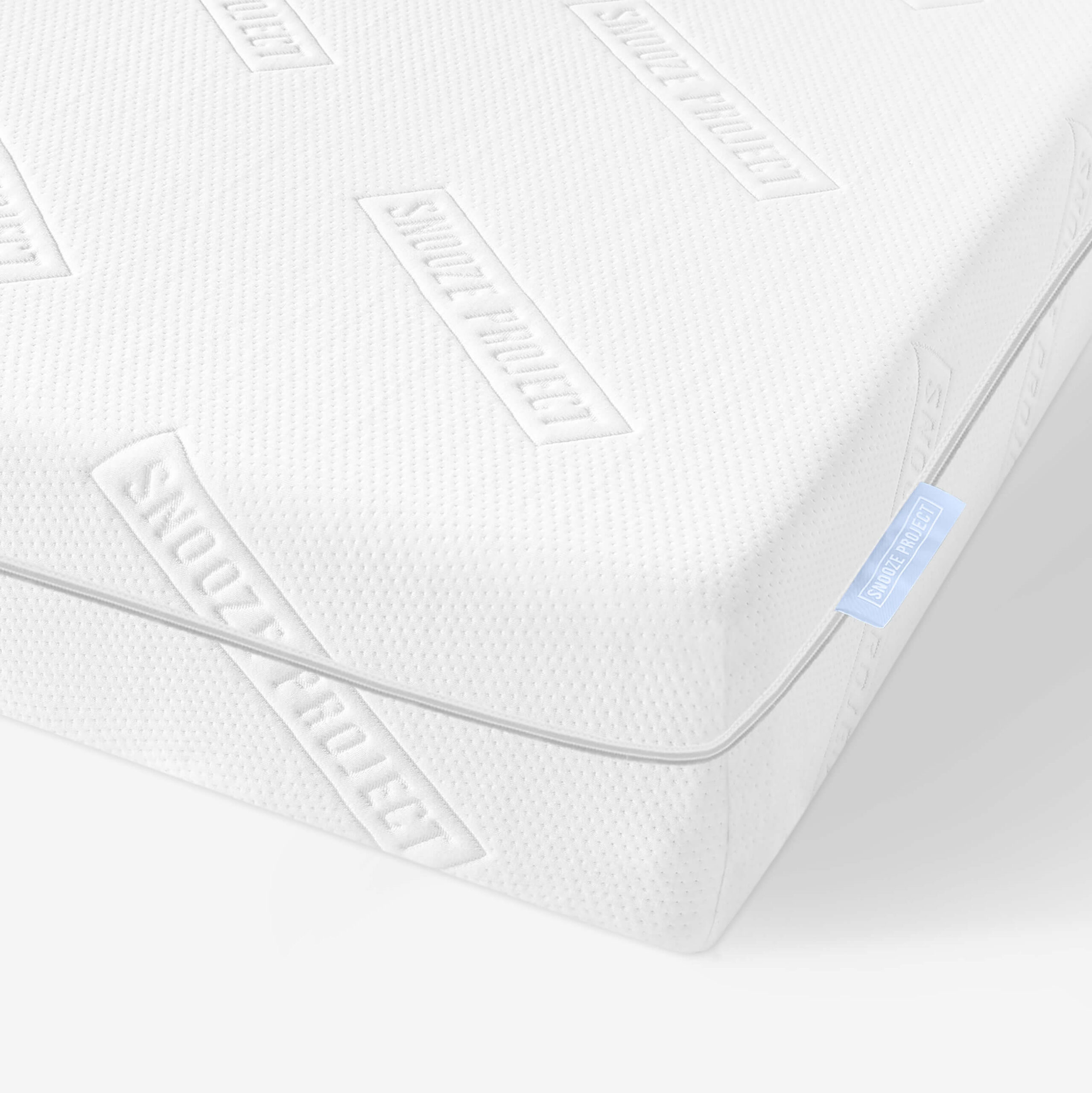 Nahaufnahme einer weißen Matratze mit einer strukturierten Oberfläche und dem mehrfach eingeprägten Schriftzug SNOOZE PROJECT. An der Seite der Matratze ist ein hellblaues Stoffschild mit weißem Text angebracht.