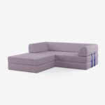 Ein modernes, hellviolettes Sektionssofa mit gerippter Struktur und blauen Gurtdetails auf einer Seite, vor einem schlichten weißen Hintergrund.