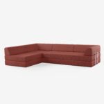 Ein modernes, L-förmiges Sektionssofa, bezogen mit einem rötlich-braunen Stoff, mit klaren Linien und niedrigen Rückenlehnen. Das Sofa steht auf einem weißen Hintergrund und ist mit minimalistischen Kissen im Blockstil ausgestattet.